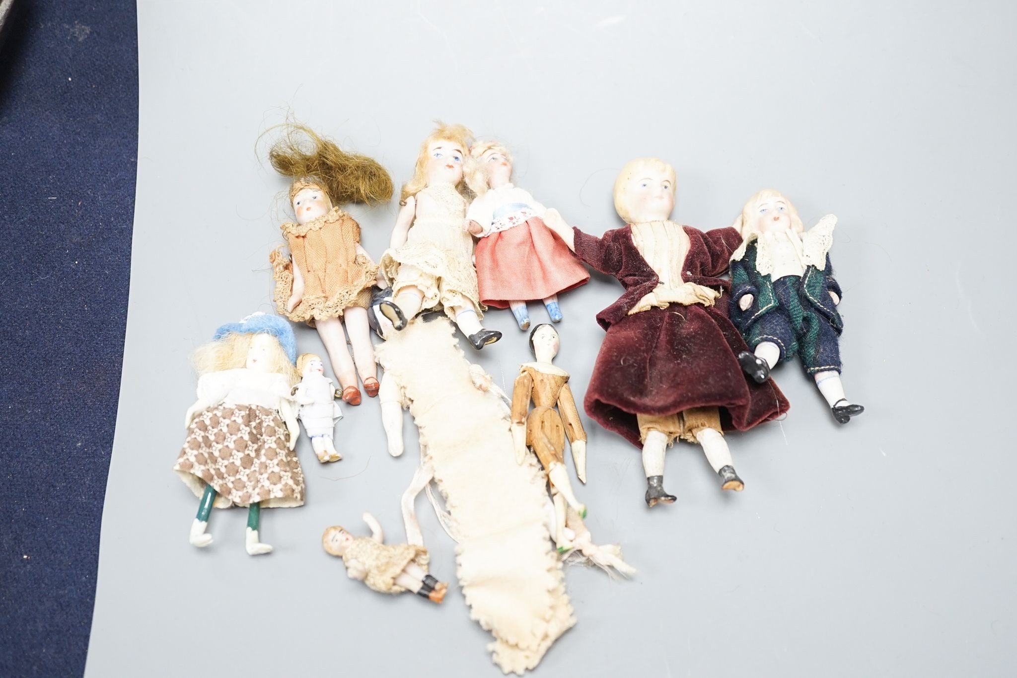 A collection of miniature bisque dolls and another larger doll in a wooden cradle, 11 dolls in total., Cradle 23.5 cms long.